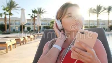 穿着红色比基尼、带着白色耳机听智能<strong>手机音乐</strong>的年轻迷人的微笑少女的肖像